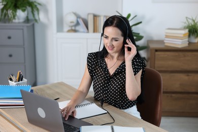 Photo of Woman in headset passing online test on laptop at table indoors