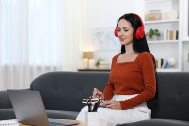 Photo of Woman taking notes while passing online test via laptop at home