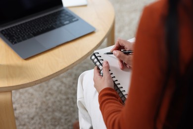 Photo of Woman taking notes while passing online test via laptop at home, closeup