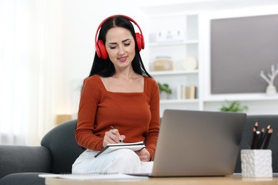 Photo of Woman taking notes while passing online test via laptop at home