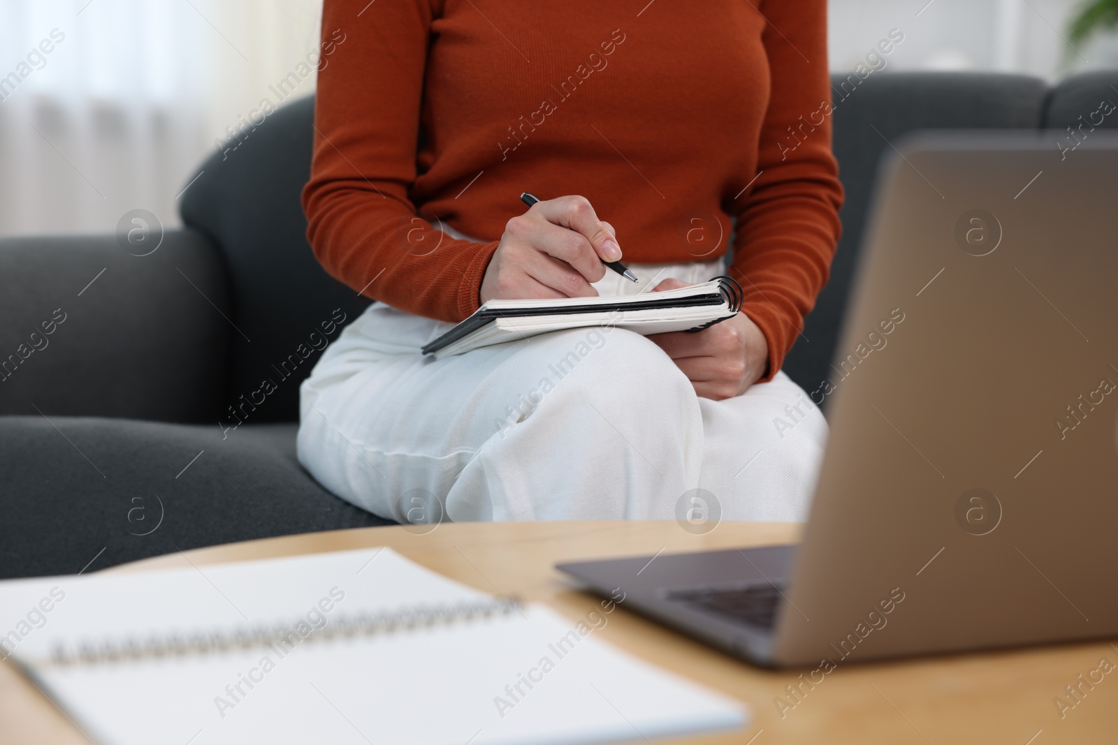 Photo of Woman taking notes while passing online test via laptop at home, closeup