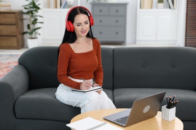 Photo of Woman taking notes while passing online test via laptop at home