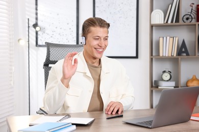 Photo of Man in headset passing online test via laptop at table indoors