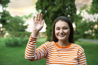Photo of Happy young woman waving goodbye in park