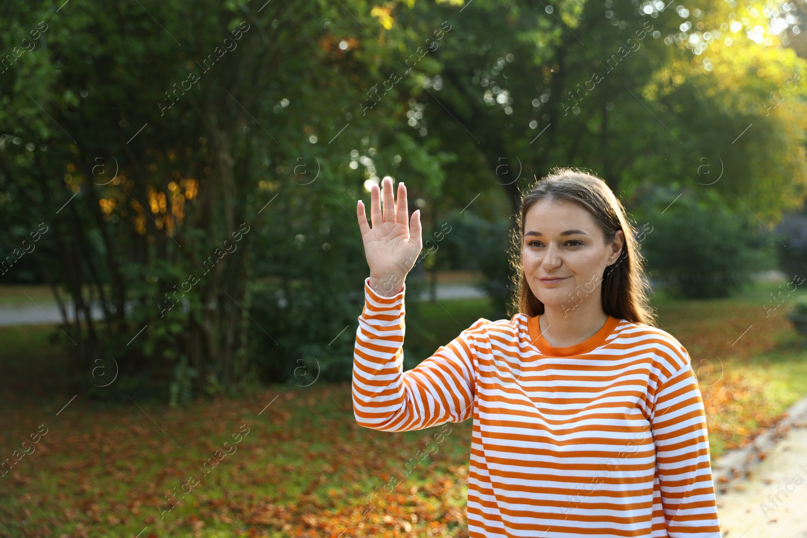 Photo of Young woman waving goodbye in park, space for text