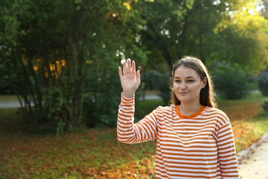Photo of Young woman waving goodbye in park, space for text