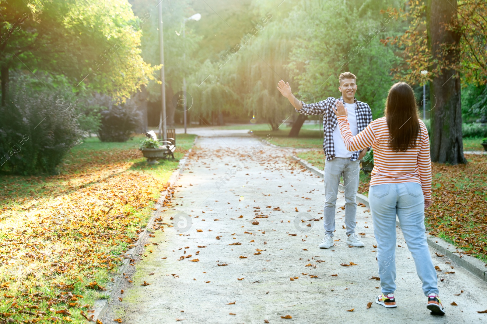 Photo of Woman waving goodbye to her friend in park, back view