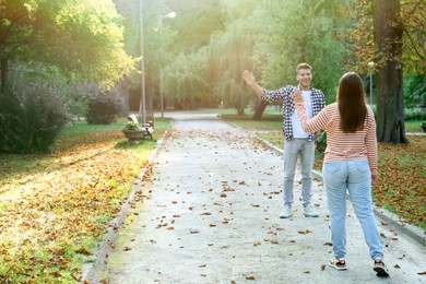 Photo of Woman waving goodbye to her friend in park, back view