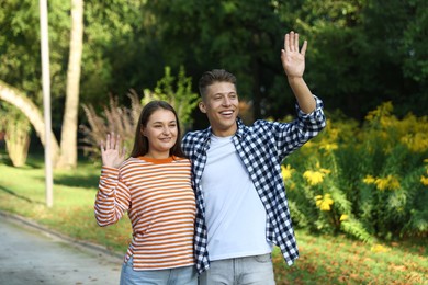 Photo of Couple waving goodbye in park on sunny day