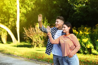 Photo of Couple waving goodbye in park on sunny day, space for text