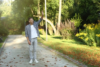 Photo of Happy young man waving goodbye in park, space for text