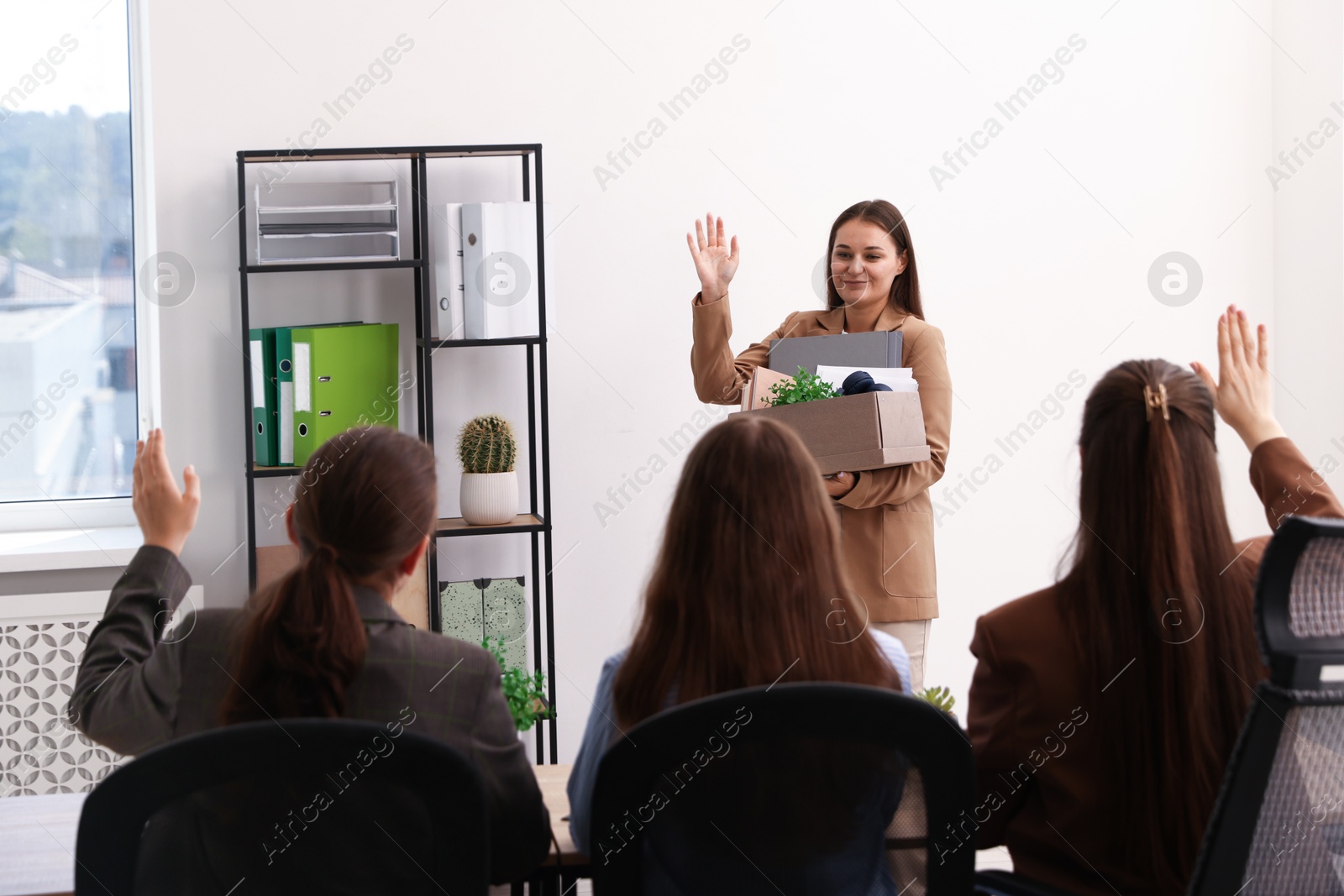 Photo of Woman with stuff waving goodbye to her colleagues in office