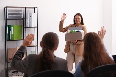 Photo of Woman with stuff waving goodbye to her colleagues in office