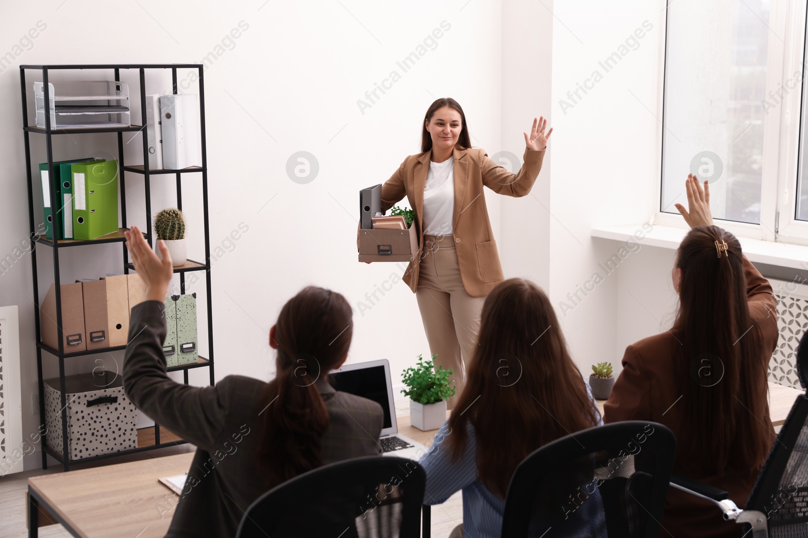 Photo of Woman with stuff waving goodbye to her colleagues in office