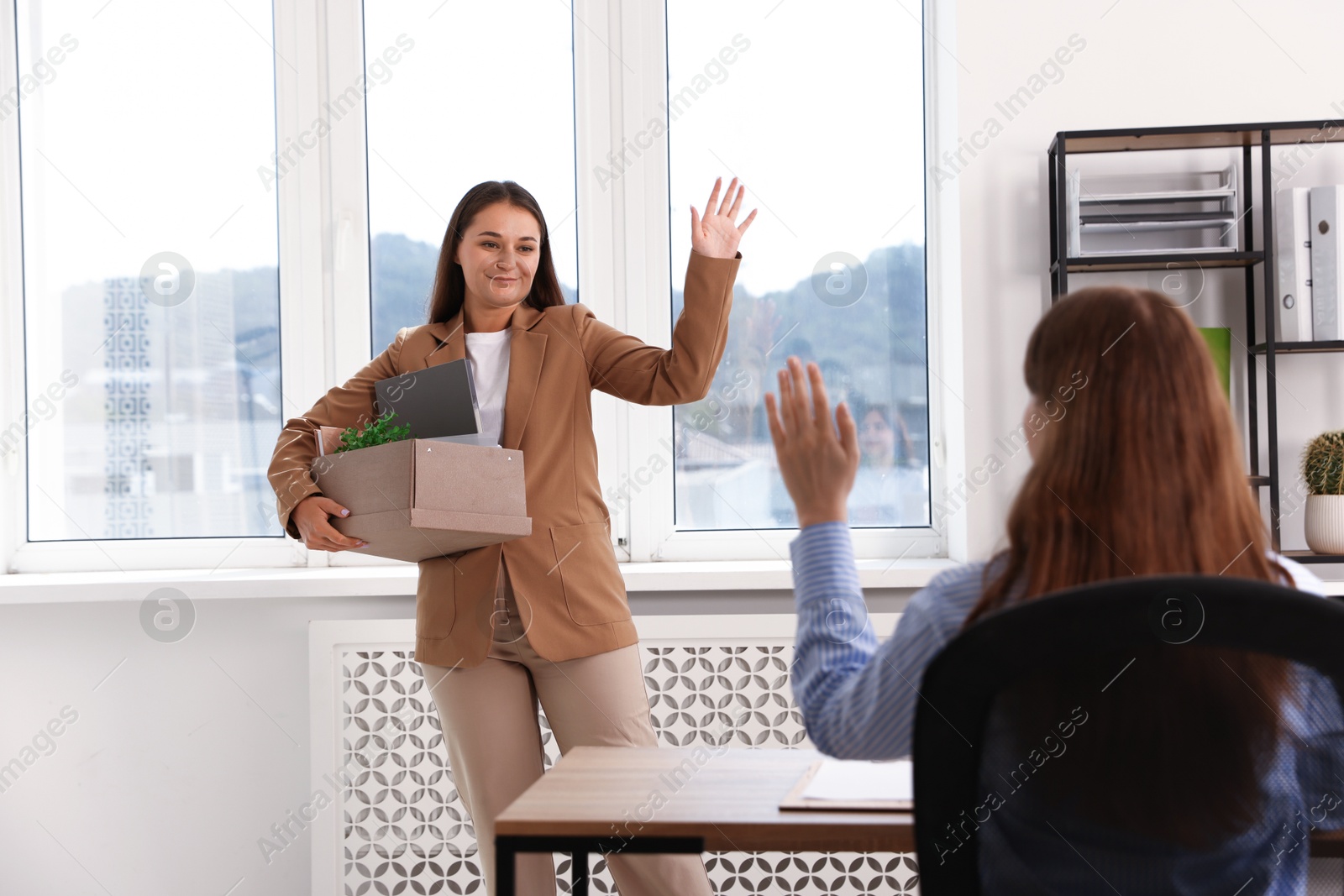 Photo of Woman with stuff waving goodbye to her colleague in office