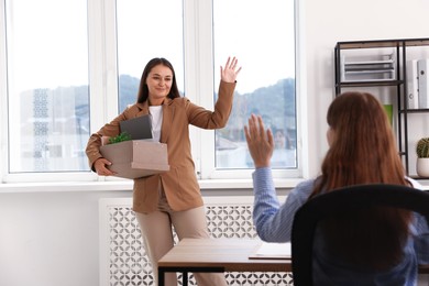 Photo of Woman with stuff waving goodbye to her colleague in office