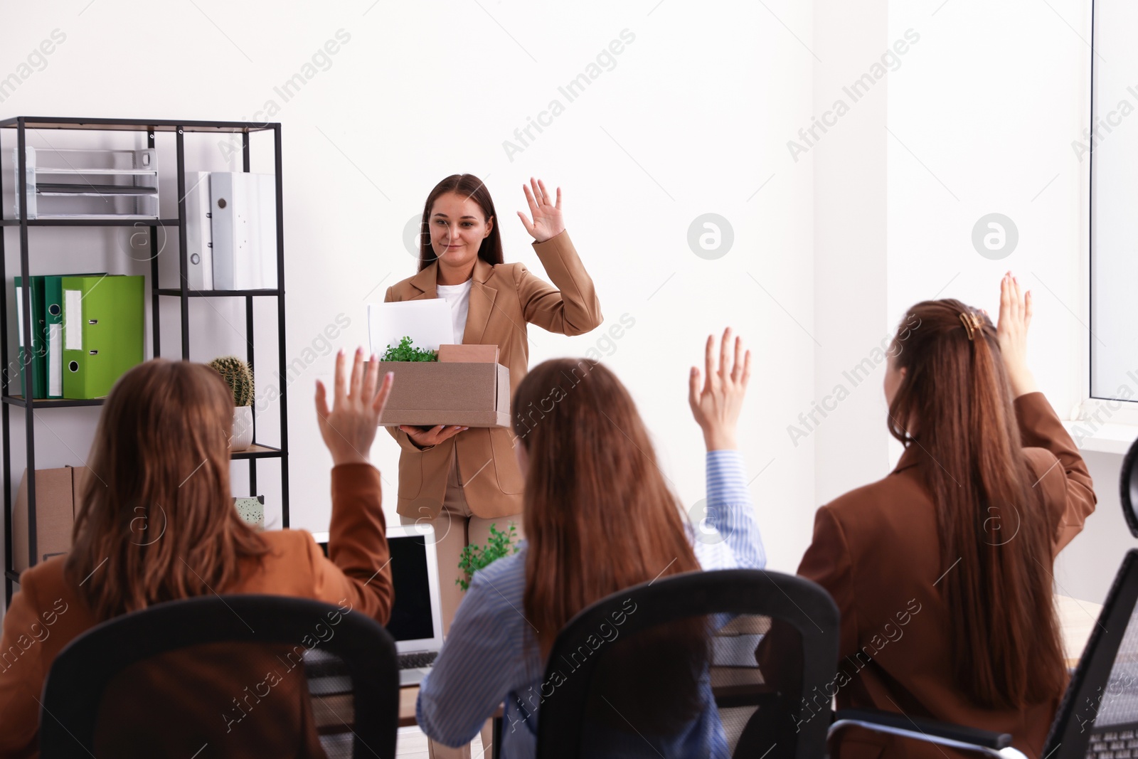 Photo of Woman with stuff waving goodbye to her colleagues in office