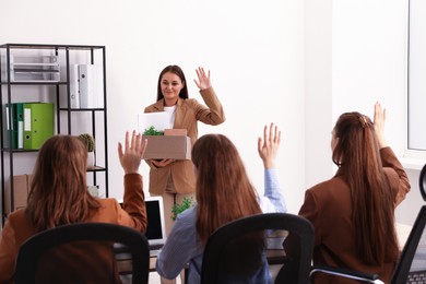 Photo of Woman with stuff waving goodbye to her colleagues in office