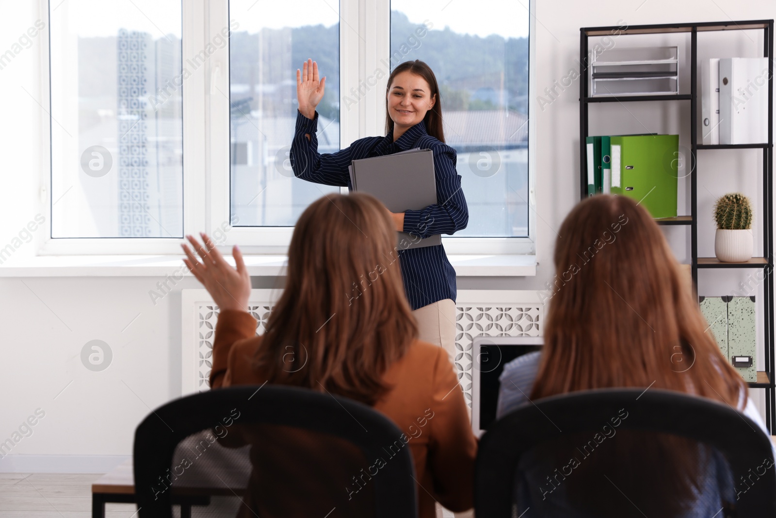Photo of Woman with folders waving goodbye to her colleagues in office