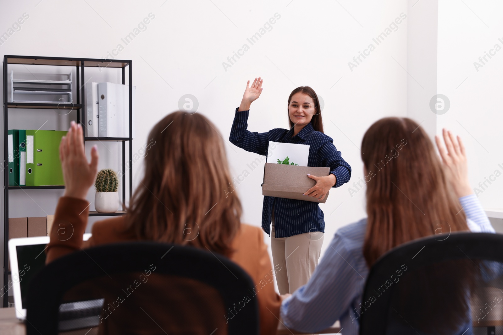 Photo of Woman with stuff waving goodbye to her colleagues in office