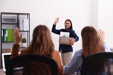 Photo of Woman with stuff waving goodbye to her colleagues in office