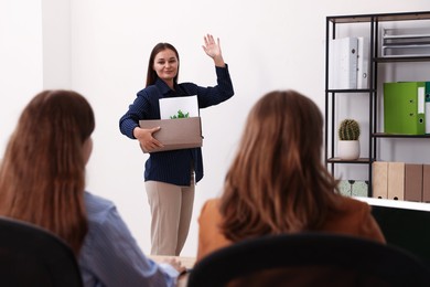 Photo of Woman with stuff waving goodbye to her colleagues in office
