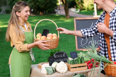 Photo of Man choosing fresh apples from stall with vegetables at farmer's market