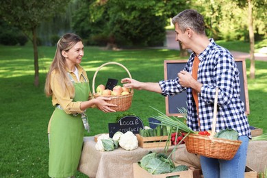 Photo of Man choosing fresh apples from stall with vegetables at farmer's market