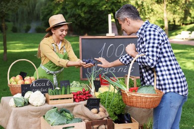 Photo of Man choosing fresh plums from stall with vegetables at farmer's market