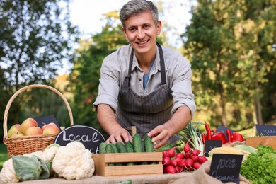 Photo of Farmer near stall with different fresh vegetables at market