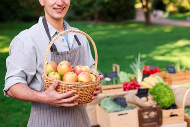 Photo of Farmer with apples in wicker basket near stall market, closeup