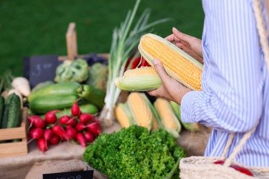 Photo of Woman choosing fresh vegetables from stall at farmer's market, closeup