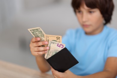 Photo of Boy with pocket money at wooden table indoors, selective focus