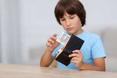Photo of Boy with pocket money at wooden table indoors, selective focus. Space for text