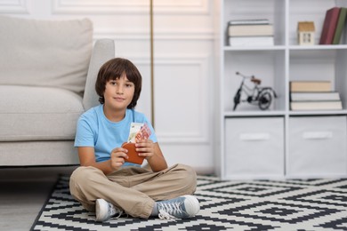 Photo of Boy with pocket money on floor at home. Space for text