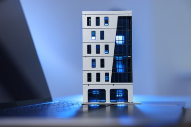 Photo of Real estate. Apartment building model and laptop on table in color light, closeup