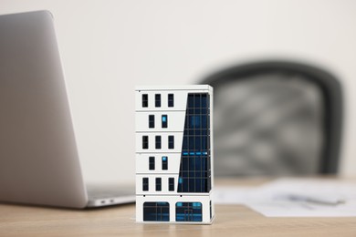 Photo of Real estate. Apartment building model, paperwork and laptop on wooden table indoors, closeup