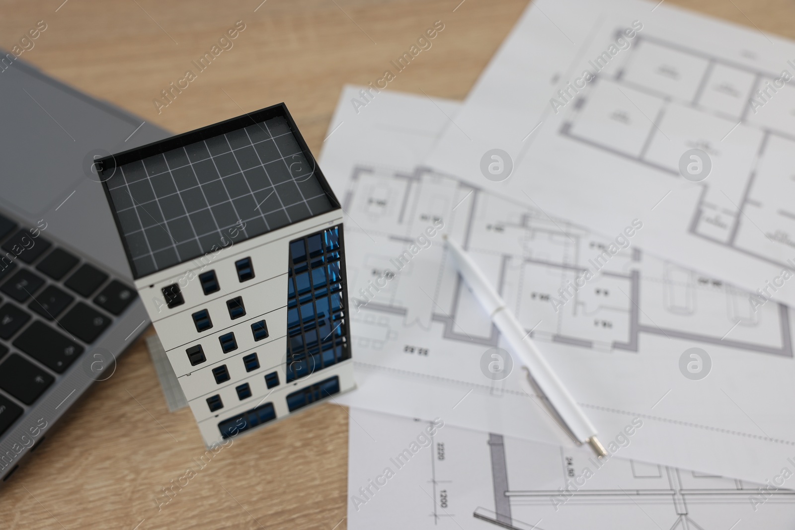 Photo of Real estate. Apartment building model, architectural drawings, laptop and pen on wooden table, closeup