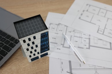 Photo of Real estate. Apartment building model, architectural drawings, laptop and pen on wooden table, closeup