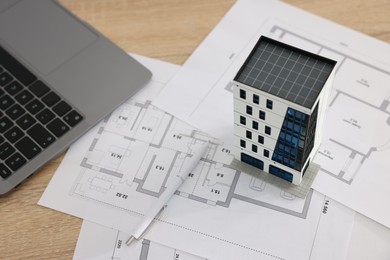 Photo of Real estate. Apartment building model, architectural drawings, laptop and pen on wooden table, closeup