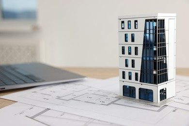 Photo of Real estate. Apartment building model, architectural drawings and laptop on table, closeup. Space for text
