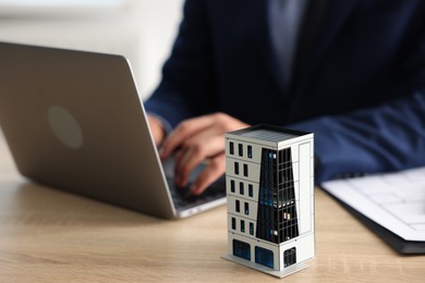 Photo of Real estate agent working with laptop at wooden table, focus on apartment building model