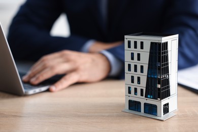 Photo of Real estate agent working with laptop at wooden table, focus on apartment building model