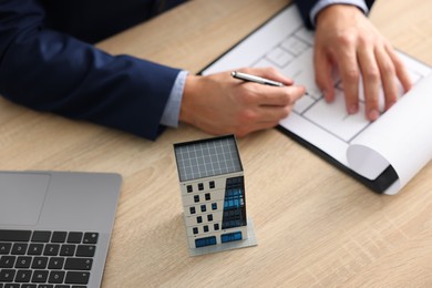 Photo of Real estate agent with architectural drawing, apartment building model and laptop at wooden table, above view