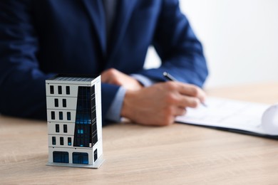 Photo of Real estate agent with paperwork at wooden table, focus on apartment building model