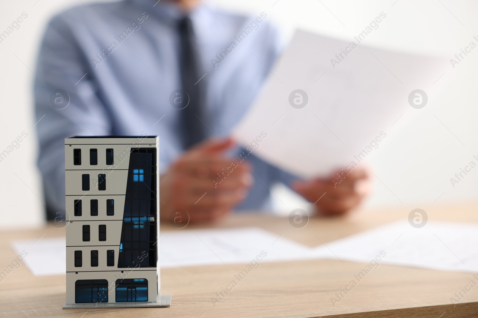Photo of Real estate agent with paperwork at wooden table, focus on apartment building model