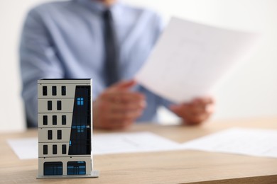 Photo of Real estate agent with paperwork at wooden table, focus on apartment building model