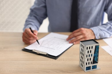 Photo of Real estate agent with paperwork at wooden table, focus on apartment building model