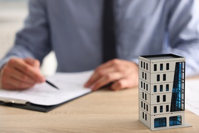 Photo of Real estate agent with paperwork at wooden table, focus on apartment building model
