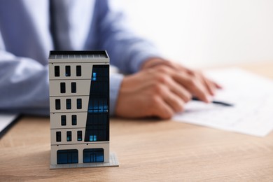 Photo of Real estate agent with paperwork at wooden table, focus on apartment building model